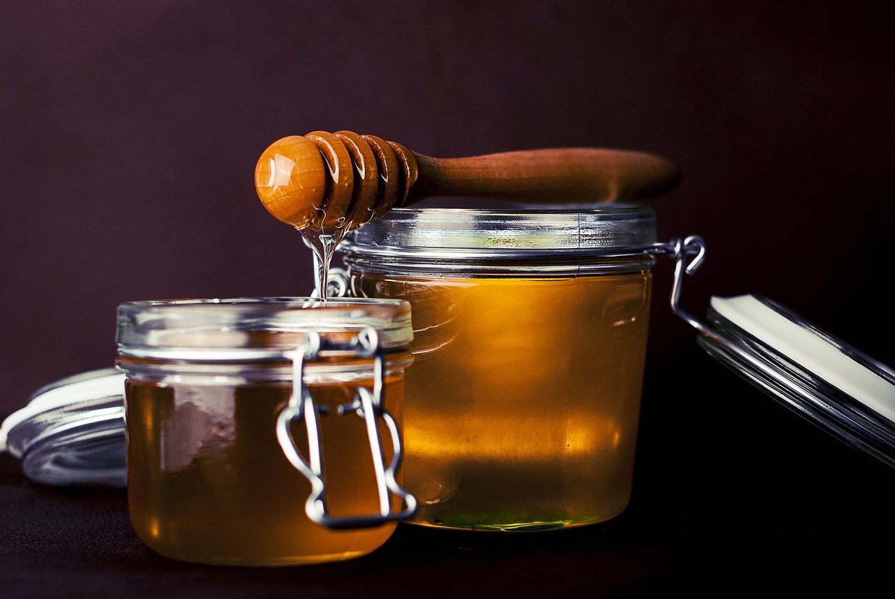 Honey dripping from a wooden dipper into two glass jars
