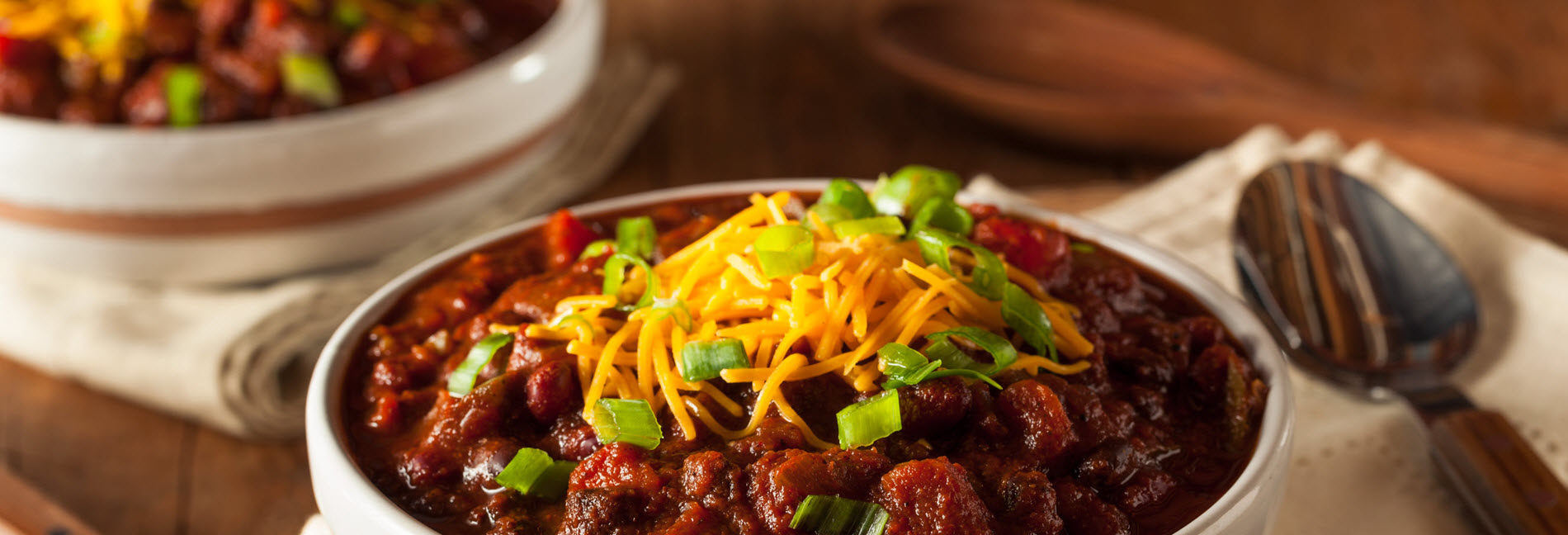 A bowl of red chili topped with cheddar and green onion