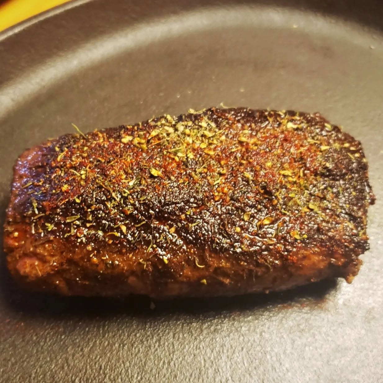 Seasoned steak with a dark crust in a skillet